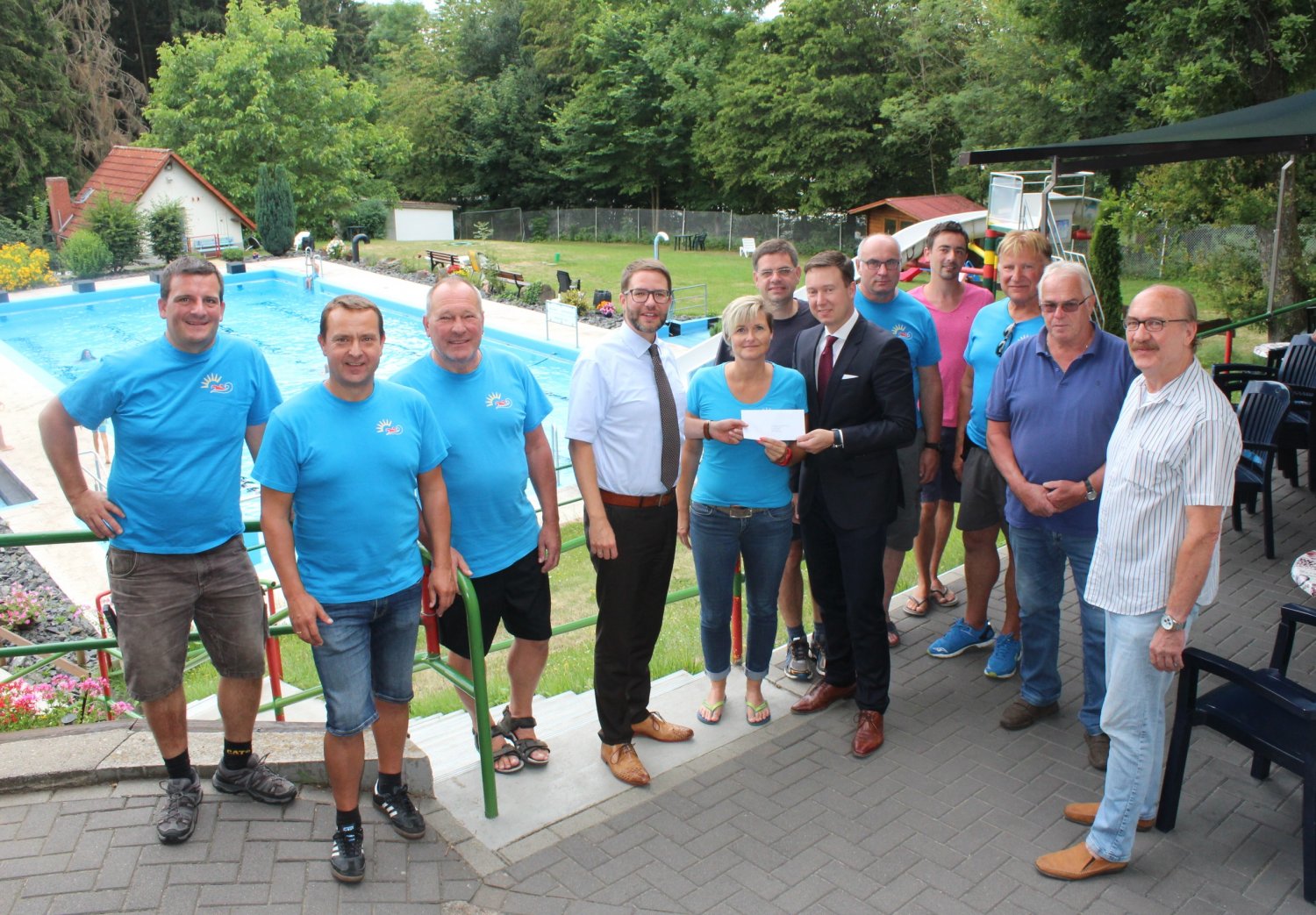 „Es besteht Handlungsbedarf im Freibad Hutten“: Landrat Thorsten Stolz (Vierter von links) übergibt den Zuwendungsbescheid des Kreises für die Sanierungsmaßnahmen an Nicole Winhold, Schatzmeisterin des Fördervereins, sowie an Bürgermeister Matthias Möller