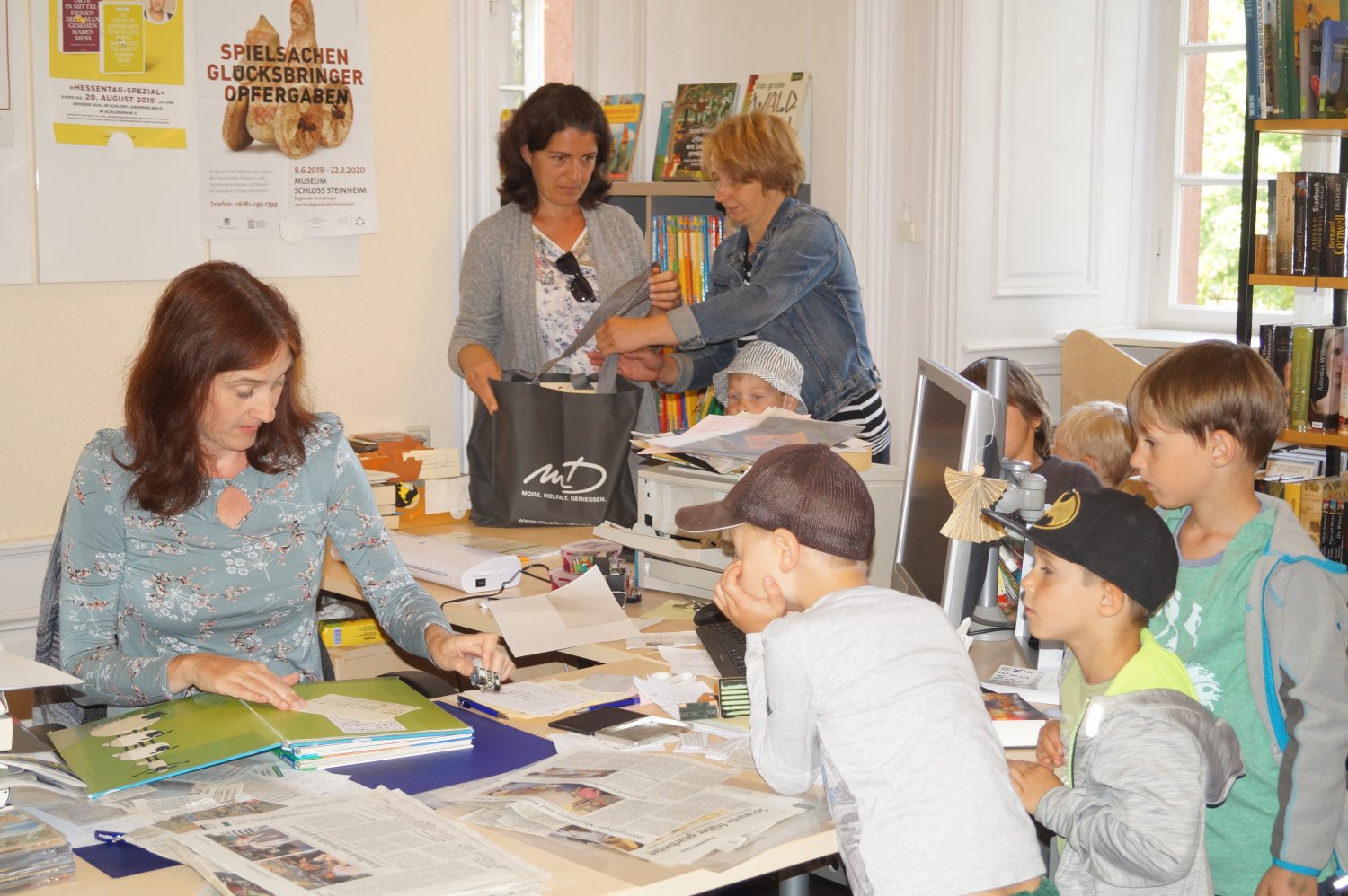 Bibliotheksleiterin Christiane Halsch an ihrem Schreibtisch zusammen mit den Kindern der Kita Pusteblume.