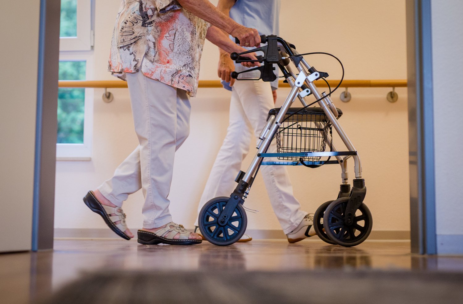 Eine Pflegekraft geht in einem Pflegeheim mit einer älteren Dame über einen Korridor