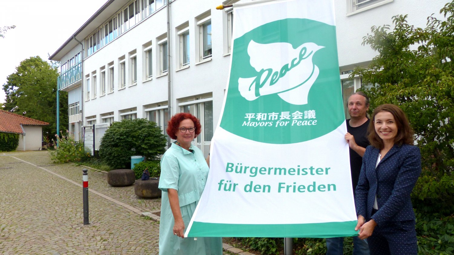 Bürgermeisterin Monika Böttcher hat gemeinsam mit Kommunalpolitiker*innen am Rathaus der Stadt Maintal die Flagge des Bündnisses Mayors for Peace / Bürgermeister für den Frieden gehisst