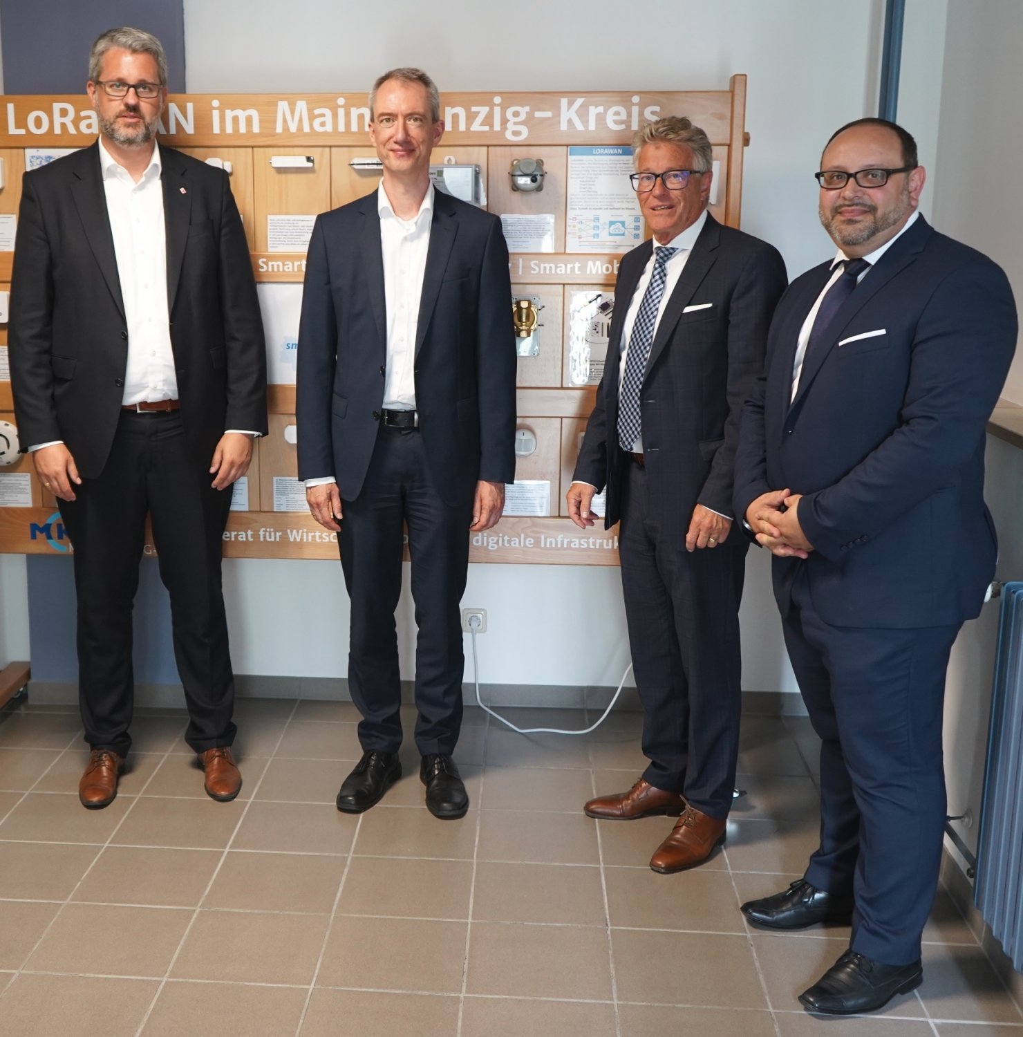 Staatssekretär Patrick Burghardt, Ministerialdirigent Marcus Milas, Kreisbeigeordneter Winfried Ottmann sowie Pietro Pitruzzella an der Demonstrationswand zu LoRaWan.