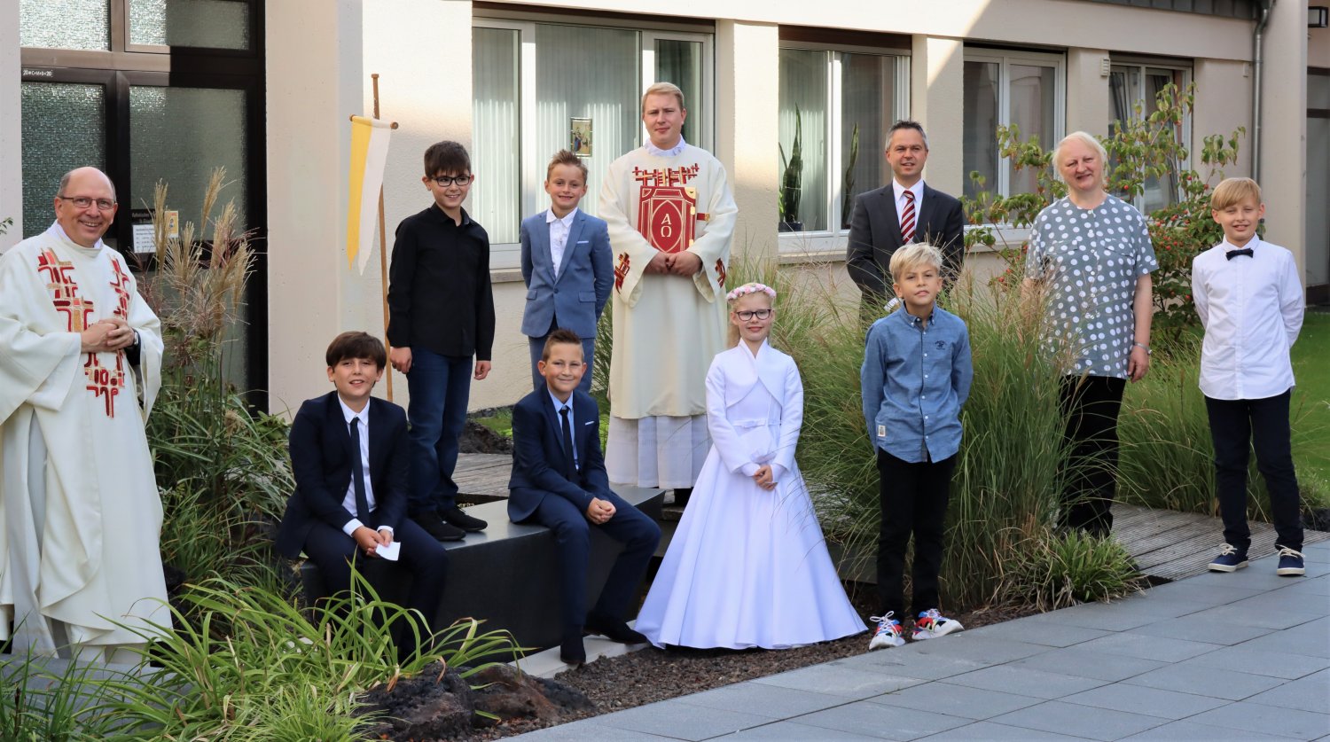 Die Kinder aus Mittel- und Wachenbuchen in zwei Gruppen am Tag ihrer Erstkommunion in zwei verschiedenen Feiern auf der Schiffsskulptur am Bachlauf des Kesselstädter Kirchplatzes.