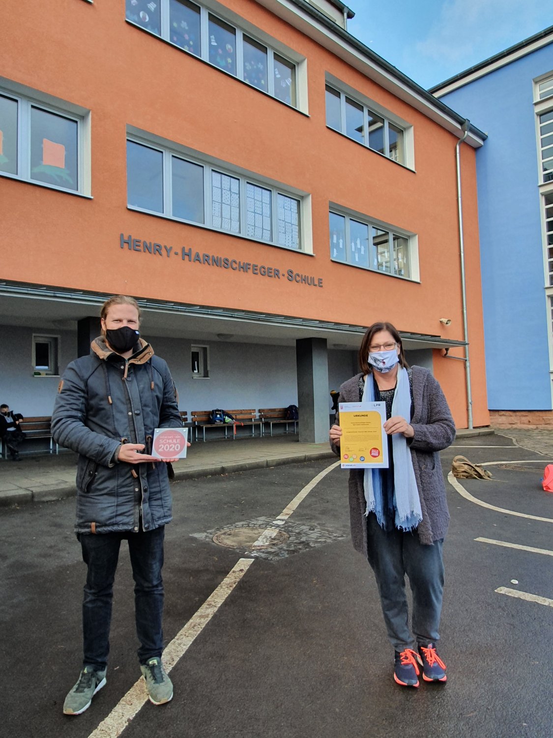 Vor dem Grundschulgebäude: die Lehrkräfte Lucas Ruppel und Katja Eckert mit dem Siegel „Internet-ABC-Schule“
