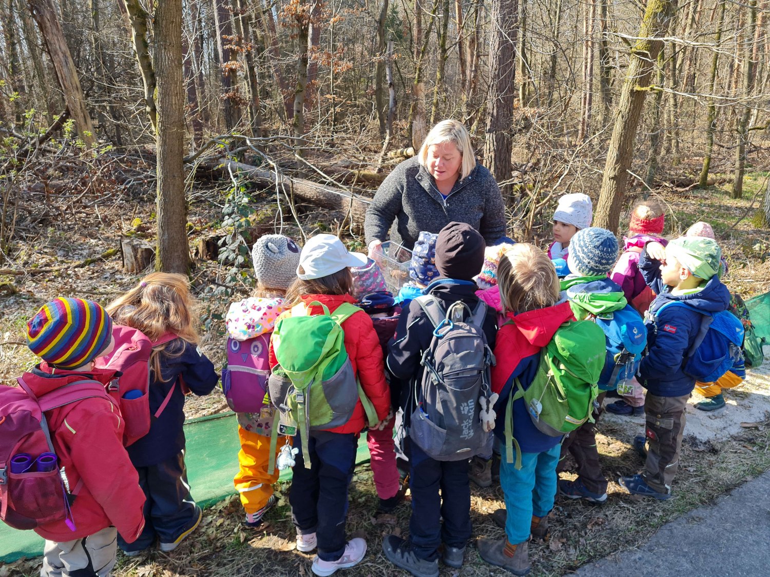 Erzieherin Heike Altinger zeigt den Kindern der Waldgruppe „Die Weltenbummler*innen“, was sich in den Eimern entlang des Amphibienzauns befindet. Insgesamt sieben Erdkröten brachten die Kinder an diesem Tag sicher zum Laichgewässer.