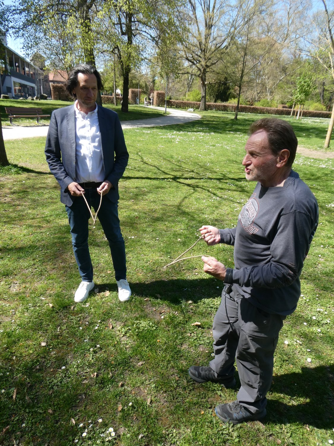 Wolfgang Schaffert (rechts) kann im Schlossgarten HIS-Betriebsleiter Markus Henrich mit Hilfe seiner Wünschelrute rasch eine Stelle bestimmen, die sich für das Bohren eines Brunnens eignet. 