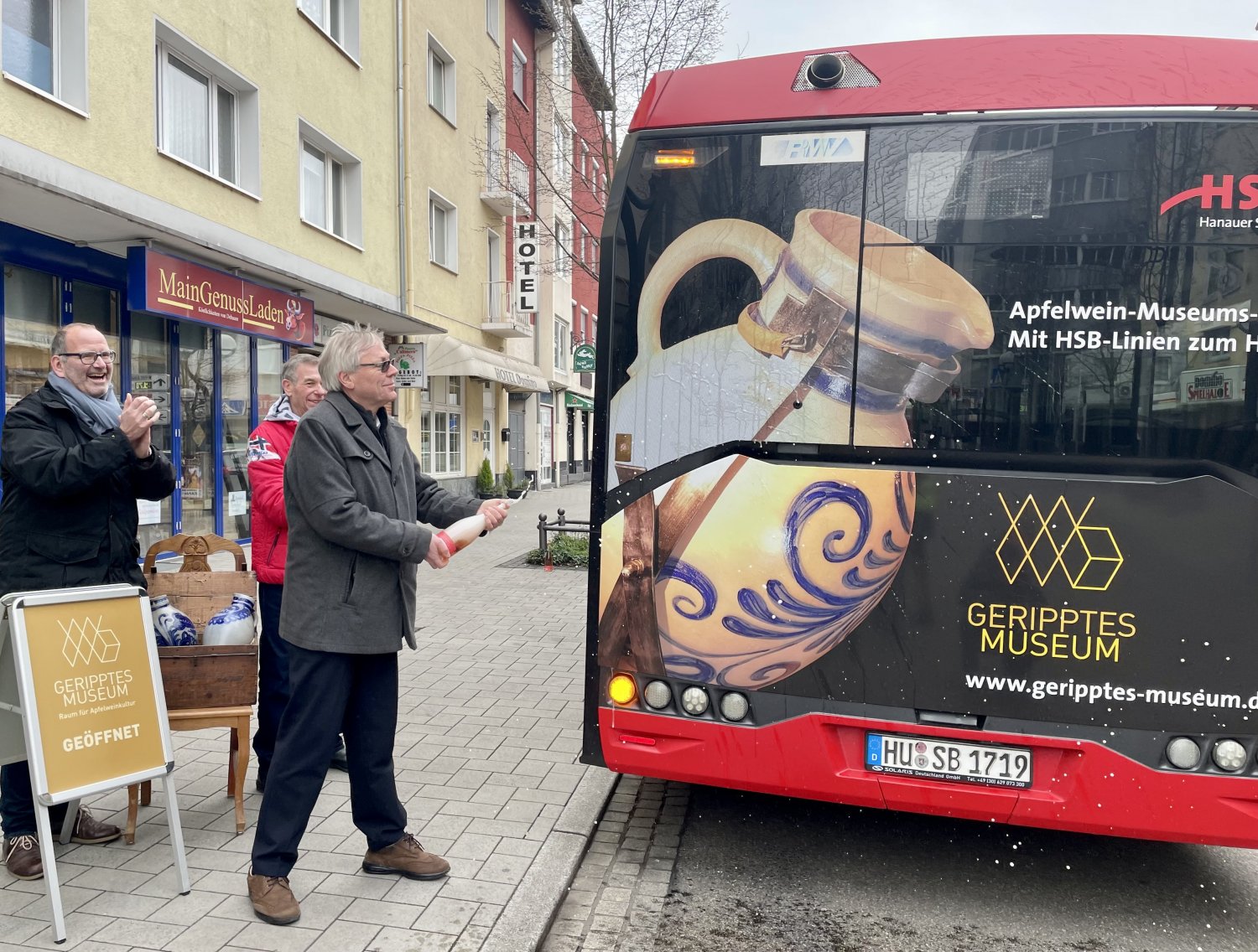 HSB-Geschäftsführer Thomas Schulte tauft den Bus mit dem Foto des Größten Bembel der Welt am Heck vor dem Gerippten Museum am Hanauer Heumarkt, assistiert von Uwe Berndt (links) und Thomas Seifert von Trägerverein des Apfelweinmuseums.