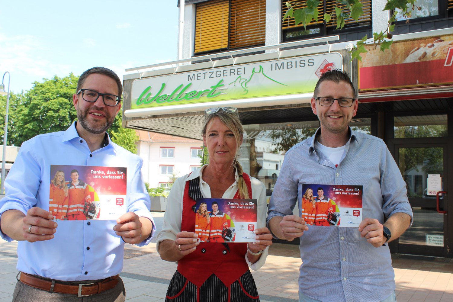 Landrat Thorsten Stolz (links) überbringt kostenloses Werbematerial für die Aktion „Rettungsgasse an der Kasse“ an Christian Dadt und an Sabine Bowyer.