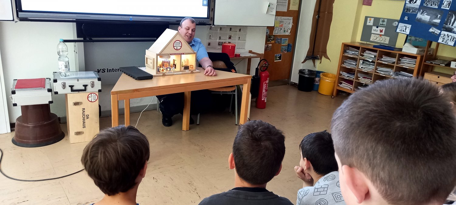 Mithilfe des Rauchhauses erklärt Brandschutzerziehungskoordinator Oliver Groß den Kindern der 3a der Ysenburgschule, welchen großen Effekt geschlossene Zimmertüren im Falle eines Brandes haben.