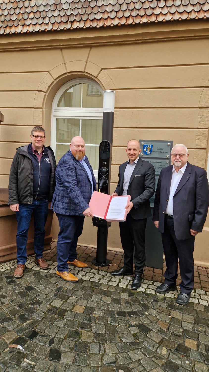von links: Florin Oswald und der Geschäftsführer der Qwello Deutschland GmbH Christian Kozur präsentieren mit Bürgermeister Dominik Brasch und Ersten Stadtrat Werner Wolf den unterzeichneten Gestattungsvertrag vor einer Qwello Ladesäule.