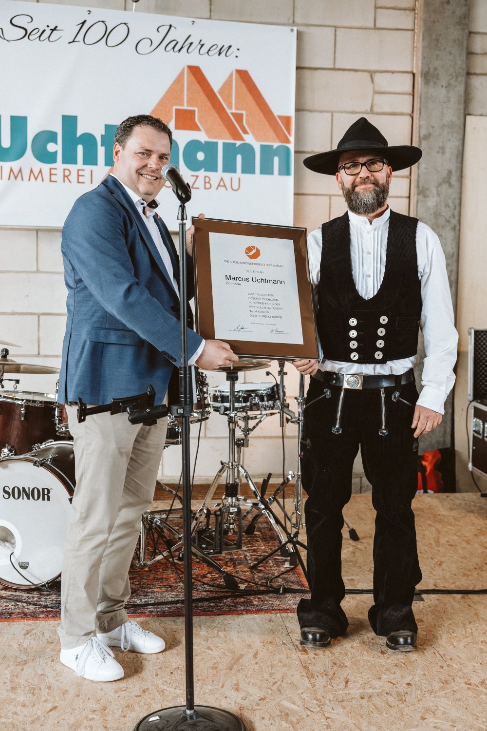 Obermeister Bastian Lotz (links) überreicht Betriebsinhaber Marcus Uchtmann die Ehrenurkunde der Kreishandwerkerschaft Hanau zum 100-jährigen Betriebsjubiläum