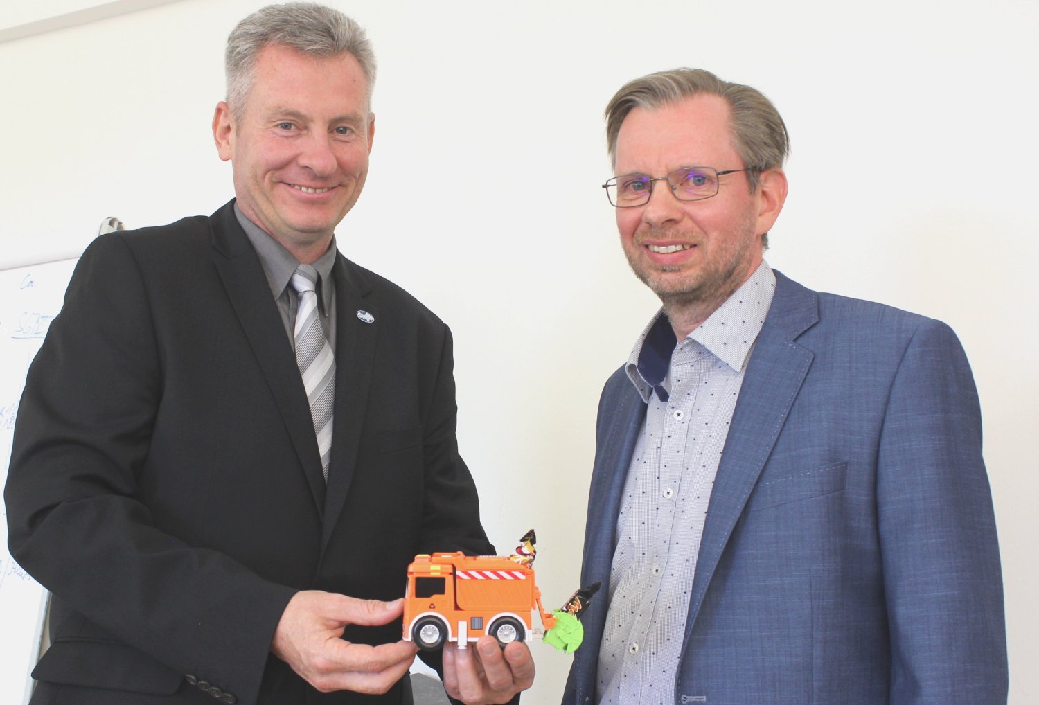 Erster Kreisbeigeordneter Andreas Hofmann überreicht dem neuen Leiter des Eigenbetriebs Abfallwirtschaft des Main-Kinzig-Kreises zum Dienstantritt ein Miniatur-Müllfahrzeug mit Pressvorrichtung.