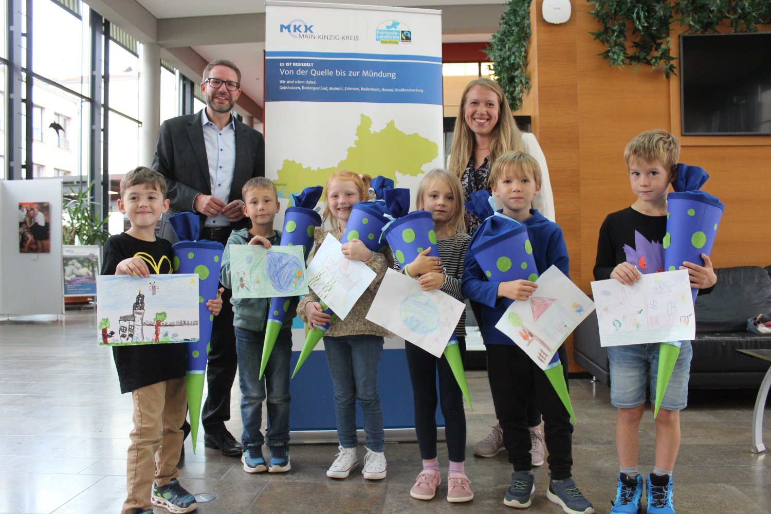 Landrat Thorsten Stolz gemeinsam mit Stefanie Häuser, Fairtrade-Beauftragte des Main-Kinzig-Kreises und den Kindern, die ihre Bilder und Schultüten zeigen.
