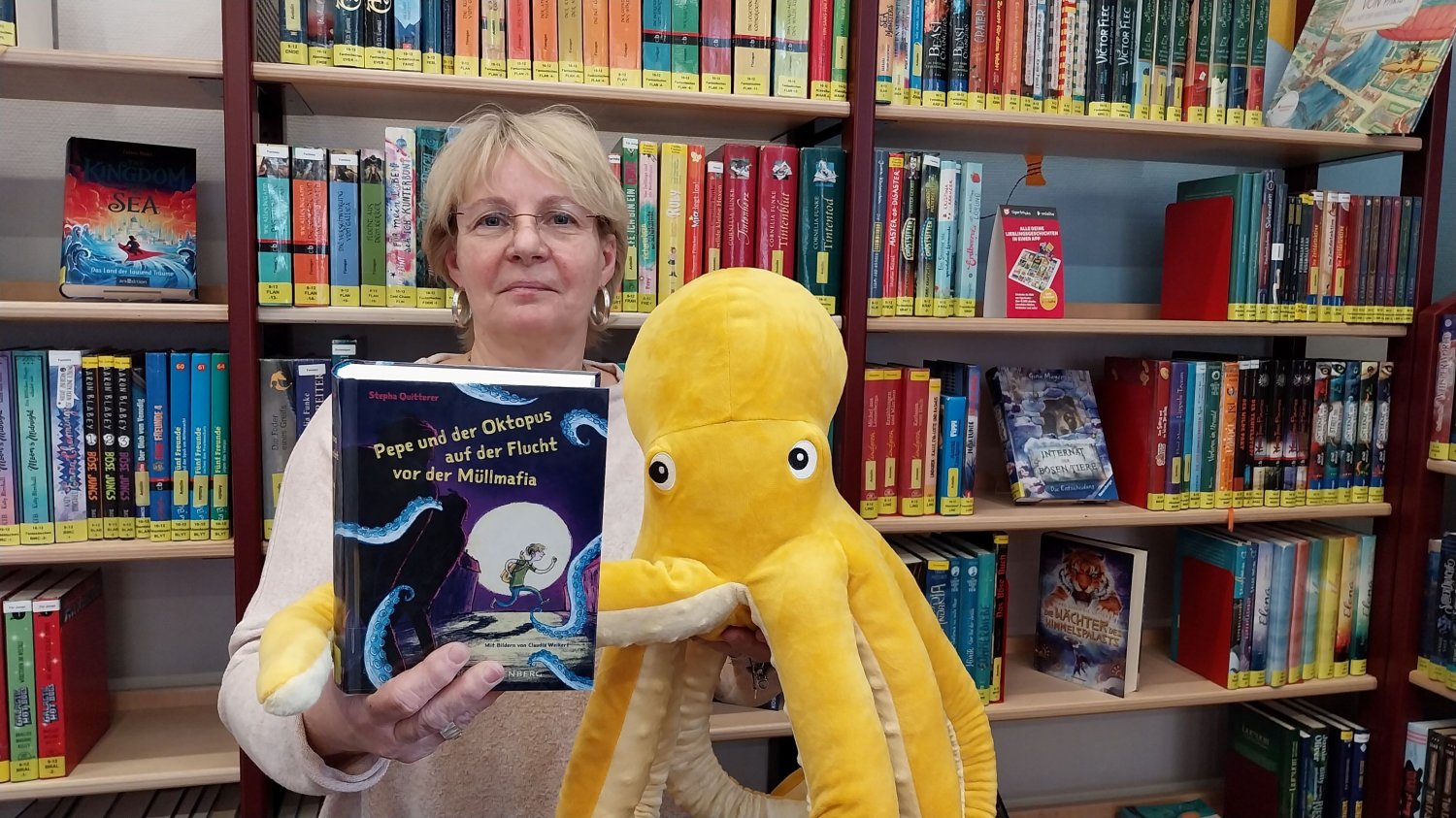 Büchereileiterin Claudia Beck und der achtarmige Botschafter der Weltmeere werben für das Lesen des Umweltkrimis und die Teilnahme am Gewinnspiel.