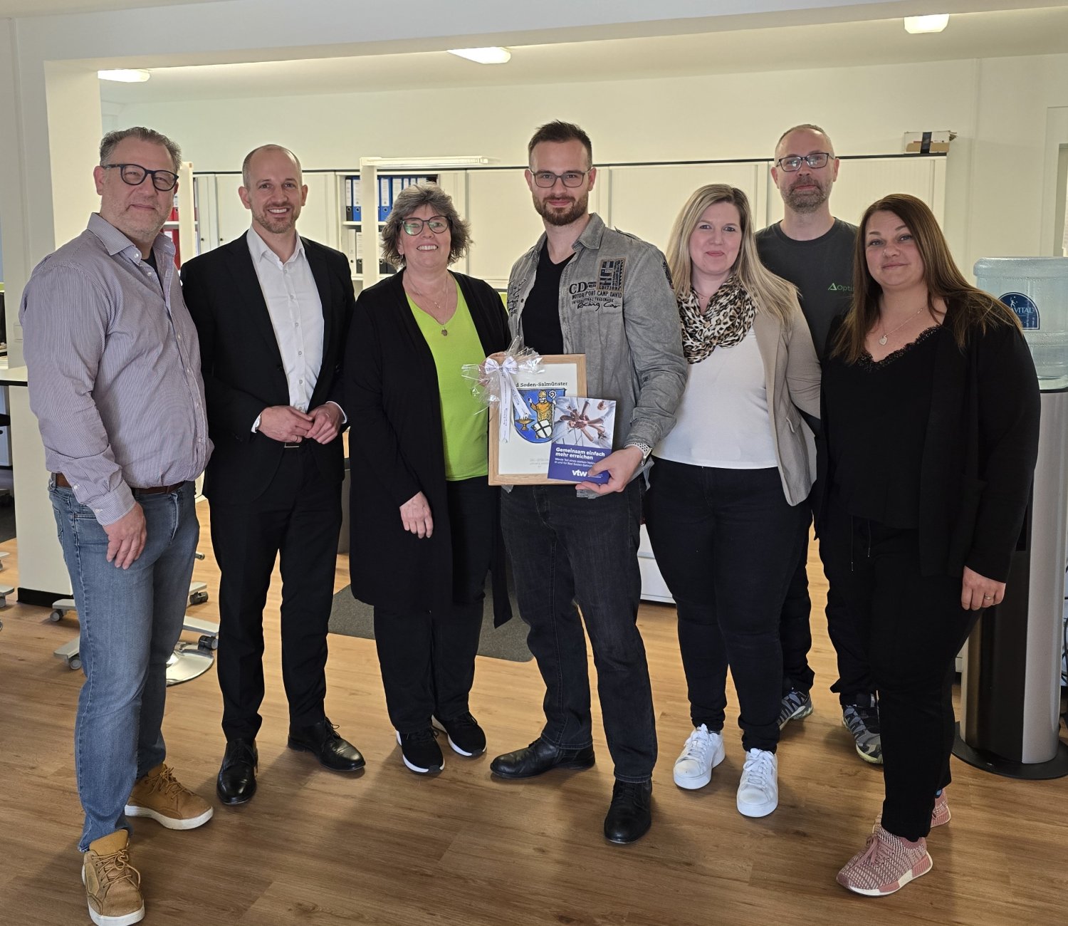Geschäftsführer Mario Vajcek (links), Bürgermeister Dominik Brasch, Marius Vajcek (Mitte mit Bild) und Mitarbeiterschaft am neuen Standort der Firma Optima in Salmünster