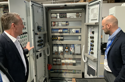 Sascha Schröder und Falk Ritzau vor einer Schaltanlage in der Produktionshalle von Scholl (v.l.)